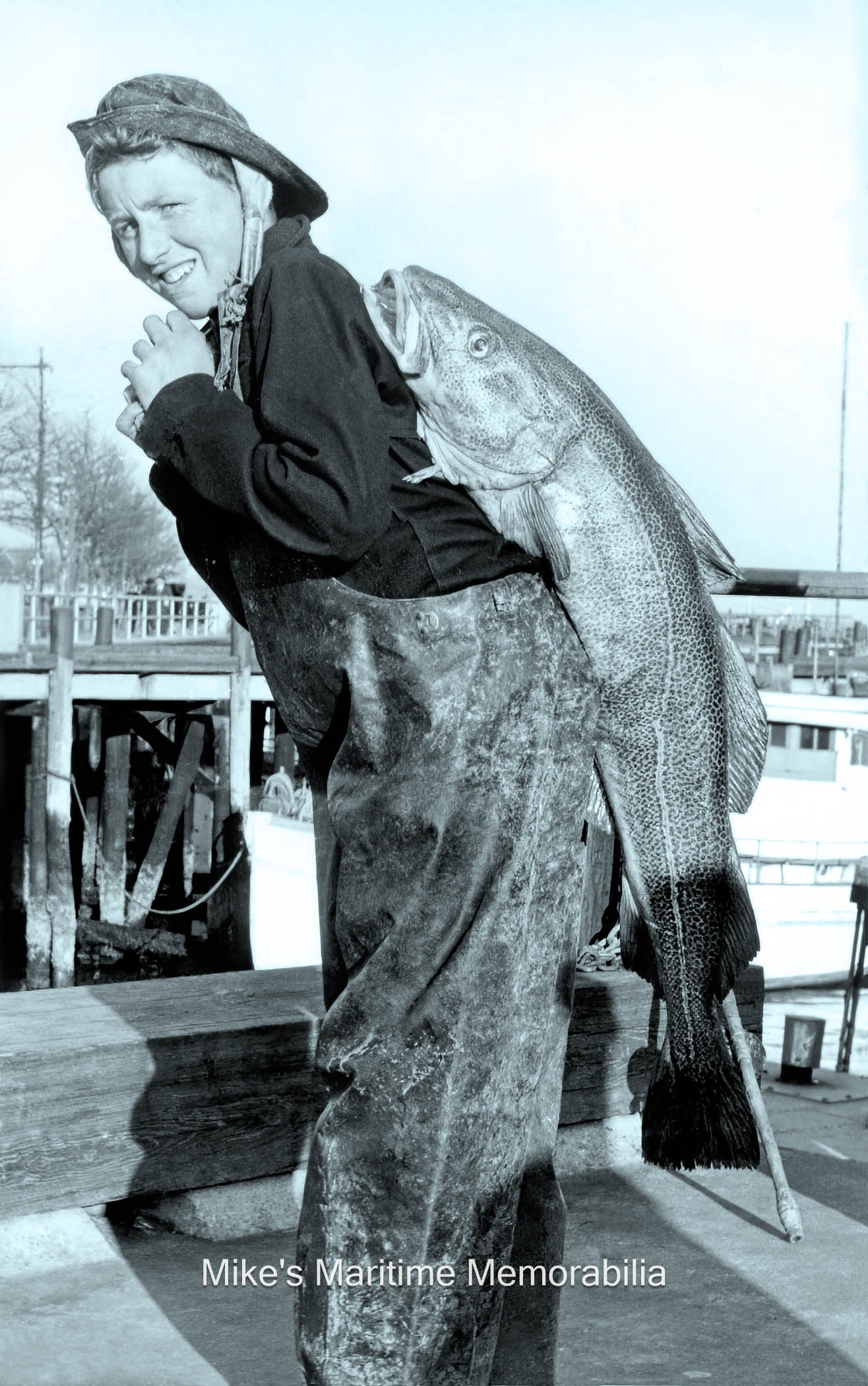 Sheepshead Bay Cod Catch – 1955 Heigh-ho, heigh-ho. Its home from work we go! Instead of swinging a sea bag over his shoulder, this Sheepshead Bay, NY party boat mate is lugging home a nice Cod for dinner circa 1955.